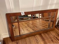 Full view of the antique pine window frame laid against a white wall on wooden flooring, showing rectangular shape with a segmented mirror insert.