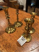 Four brass candlestick holders on a wooden table, two taller and two shorter, with a tag marked 840.