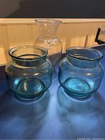 Two decorative blue-green beach glass bowls with wide mouths, and one clear tall glass vase with flared mouth and narrow neck.