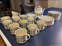 Full set arranged on table showing teapot, sugar, creamer, tea cups, saucers and dessert plates with visible Tapestry pattern and green border.