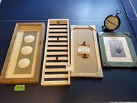 Multiple items including framed sand dollar art, wooden picture holders, a black Pottery Barn clock, and various picture frames on a blue surface.