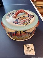 Front angle view of casserole dish showing side decoration and lid with fish motif and sculpted handle