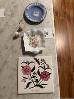 Overview showing all items on marble surface: blue Shelley dish, Wedgwood ashtray, two thimbles, and floral Johnson tile