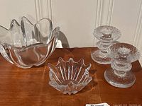 Clear glass large wavy-edged bowl, small scalloped bowl, and two textured glass candlesticks on wooden surface.