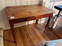 Front side view of the small harvest table showing pine wood top and reddish painted legs and drawer front with brass pull.