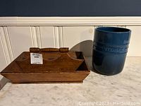 Side view showing the wooden cutlery tray with multiple compartments and handle, alongside the blue utensil holder with embossed text.