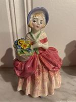 Full view of Royal Doulton 'Cissie' figurine, showing dress, bonnet, flower basket and overall shape.
