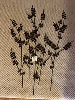 Metal willow branch wall art laid flat on carpet, showing multiple thin stems with round leaf-like accents in dark metal.