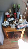 Overview of candles and holders on a wooden side table grouped together showing various types and sizes.
