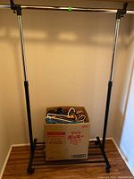 Full view of the wheeled clothing rack with a box of hangers placed on the floor underneath the rack.