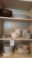 Shelves with stacks of various sized Corelle dishes, ceramic bowls, and plates including oval dishes on lower shelf.