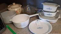 Overview of nine pieces including Corning Ware Blue Cornflower cookware, glass lid, and a large floral ceramic dish