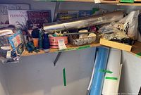 Photo showing shelf with multiple crafting books, spools of thread, ribbons, baskets of small crafting items, and two hot glue guns in box.