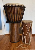 Photo of two bongo drums side by side showing size difference and details, larger with damage