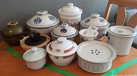 Full view of nine assorted lidded ceramic food containers on wood surface.