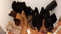 Overview photo showing eleven pairs of boots in various colors and styles including black, brown and tan with different textures, laid on a wooden floor against a white wall. Shoe horn and small cleaning set visible.