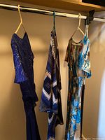 Photo of four dresses hanging on a rack including a blue abstract patterned dress, a blue and brown floral print dress, and part of two other dresses.