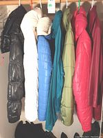 Photo showing six women's puffy jackets in black, white, blue, teal, olive green, and red on hangers.