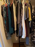 Photo showing assorted women's sweaters and tops on hangers, with a mix of patterns including animal print, stripes, solids in various colors such as teal, beige, brown, white, yellow, and black.