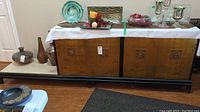 Front view of the vintage Asian style buffet cabinet showing the full length, front doors, and surface with decorative items placed on top.