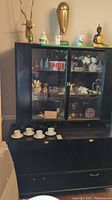Front view showing black buffet cabinet with top glass doors displaying contents, four drawers below with one missing a handle, and two lower cabinets.