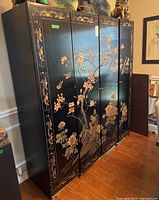 Front and side view of the black asian china cabinet with painted floral and bird motif showing overall condition and design.