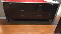Front view of dark wood dresser with nine drawers and metal handles, with glass sheet top partially covered with a cloth.