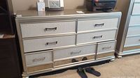 Front view of silver dresser with 7 drawers, decorative handles, and textured finish.