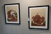 Pair of framed prints each depicting abstract masked couples in earthy tones with black frames.