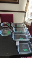Photo showing four rectangular glass baking dishes and four glass pie pans on a dark table, clearly visible and laid out for viewing.