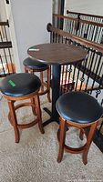 Hi-top table and three stools positioned near stair railing on carpeted floor