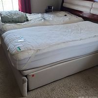Full view of the split king adjustable bed base with mattress covers and remotes, showing light beige fabric upholstery and overall condition.