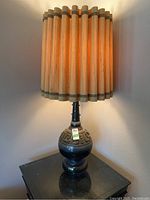 Photo of full lamp showing black carved base with geometric and animal pattern and wooden slat shade.