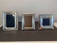 Three sterling silver picture frames placed side by side on a flat surface showing front design and shape differences.