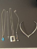 Five silver necklaces laid out on a flat surface showing variety in pendant styles and necklace types.