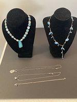 5 necklaces displayed on black stands and flat surface showing the full lot