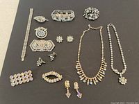 All pieces of costume jewelry arranged on dark background, showing necklaces, bracelets, brooches, and earrings with rhinestone and crystal stones.