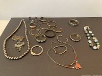 Photo showing the full assortment of costume jewelry laid flat on a dark surface, including necklaces, brooches, and various bracelets with metal, bead, and decorative stone elements.