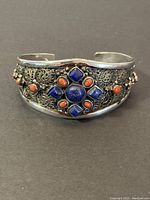 Front view of heavy sterling silver cuff bracelet showing intricate filigree and inlaid blue and red stones