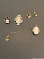 Top view of all four pieces of vintage cameo jewelry (ring, brooch, pendant necklace, earrings) on black background