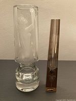 Pair of crystal vases on table, larger cylindrical vase with female figure etched, smaller rectangular vase with floral etching