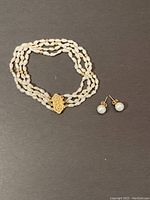 Overview of the pearl bracelet alongside the pair of pearl stud earrings on a dark background.