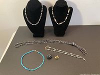 Overview of five necklaces displayed on black velvet bust and flat surface with ring and pendant laying beside them.
