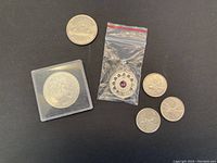 Six silver coins plus one zodiac pendant in plastic bag on black background, one coin in hard plastic case.