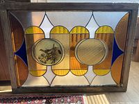 Full view of the rectangular stained glass window featuring amber, clear textured, and cobalt blue glass with a central double circular motif including a bird and nest illustration.