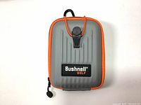 Front view of gray Bushnell Golf rangefinder case with orange zipper and black logo patch, showing clip strap secured.