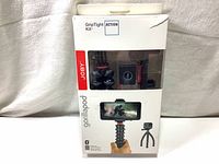 Frontal view of the Joby GorillaPod GripTight Action Kit retail box showing product inside and promotional images depicting tripod holding smartphone.