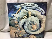 Front gatefold cover of 'A Question of Balance' record album showing detailed artwork of hands holding Earth with surrounding clouds and faces.