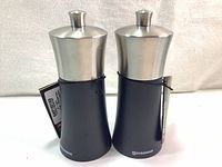 Pair of Swissmar Torre 6-inch pepper and salt mills with matte black beech wood bodies and stainless steel tops, front view.