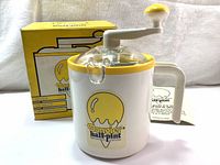 Full view of the Donvier half-pint ice cream maker in white and yellow plastic with crank and original box behind it, along with instruction booklet visible to the side.